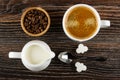 Bowl with coffee beans, cup with coffee, pitcher with milk, spoon, pieces of sugar on wooden table. Top view Royalty Free Stock Photo