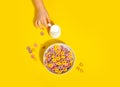 Bowl of colorful cereal corn rings on yellow table. Breakfast concept. Kid hand pouring milk into bowl Royalty Free Stock Photo