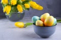 Bowl with colorful Easter eggs; spring easter decoration on gray table with bouquet of yellow tulip flowers in glass vase Royalty Free Stock Photo