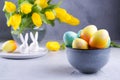 Bowl with colorful Easter eggs; spring easter decoration on gray table with bouquet of yellow tulip flowers in glass vase; Royalty Free Stock Photo