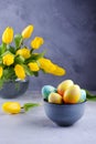 Bowl with colorful Easter eggs; spring easter decoration on gray table with bouquet of yellow tulip flowers in glass vase; Royalty Free Stock Photo