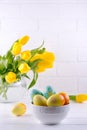 Bowl with colorful Easter eggs, spring easter decoration on white wooden table with bouquet of yellow tulip flowers in glass vase Royalty Free Stock Photo