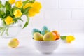 Bowl with colorful Easter eggs, spring easter decoration on white wooden table with bouquet of yellow tulip flowers in glass vase Royalty Free Stock Photo