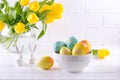 Bowl with colorful Easter eggs, spring easter decoration on white wooden table with bouquet of yellow tulip flowers in glass vase Royalty Free Stock Photo