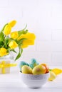 Bowl with colorful Easter eggs, spring easter decoration on white wooden table with bouquet of yellow tulip flowers in glass vase Royalty Free Stock Photo