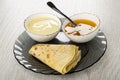 Bowl with condensed milk, spoon in bowl with honey, pancake in plate on wooden table