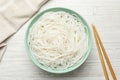 Bowl with cooked rice noodles and chopsticks on wooden table, flat lay Royalty Free Stock Photo