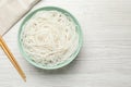 Bowl with cooked rice noodles and chopsticks on white wooden table, flat lay. Space for text Royalty Free Stock Photo