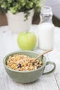 A bowl of cornflakes, an apple and a bottle of milk on a wood table