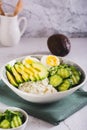 Bowl with cottage cheese, cucumber and avocado slices and boiled egg on the table vertical view