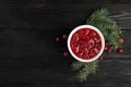 Bowl of cranberry sauce with fir tree branches on wooden background, flat lay. Royalty Free Stock Photo