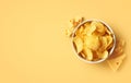 Bowl of crispy potato chips or crisps with cheese flavor on light yellow background