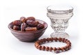 a bowl of dates, a prayer beads, a glass and a copy of the Holy Quran over white background Royalty Free Stock Photo