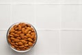 Bowl of delicious almonds on white tiled table, top view. Space for text