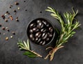 A bowl of delicious black olives, surrounded by herbs and spices, on a black stone table. Royalty Free Stock Photo