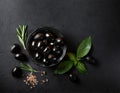 A bowl of delicious black olives, surrounded by herbs and spices, on a black stone table. Royalty Free Stock Photo