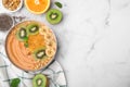 Bowl of delicious fruit smoothie with fresh banana, kiwi slices and granola on white marble table, flat lay. Space for text Royalty Free Stock Photo