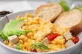 Bowl with delicious scrambled eggs, tofu and slices of baguette, closeup