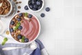 Bowl of delicious smoothie served with fresh blueberries and granola on white tiled table, flat lay. Space for text Royalty Free Stock Photo