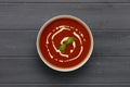 A bowl of delicious tomato soup, topped with a drizzle of cream and a sprig of basil, in a rustic bowl, shot on a distressed