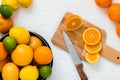 Bowl with different types of whole citruses: oranges, grapefruits, limes and lemons, and wooden board with slices of orange