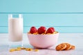 Bowl of dry cereal corn flakes with strawberry topping, chocolate chip cookies and a glass full of milk