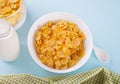 A bowl of dry corn flakes cereal with milk on blue background