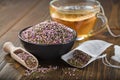 Bowl of dry healthy heather, tea bag with Ãâ¢rica flowers. Glass tea cup with herbal teabag inside on table. Herbal medicine