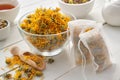 Bowl of dry marigold flowers, tea bags with dry Calendula plants. Tea cup and tea kettle on table. Alternative medicine Royalty Free Stock Photo