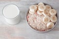 Bowl of dry oat flakes oatmeal with dry berries and sliced banana and glass of wilk on wooden table.