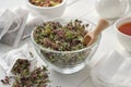 Bowl of dry Origanum vulgare flowers, tea bags filled with wild marjoram flowers. Tea cup and teapot on wooden table.