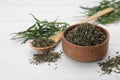 Bowl of dry tarragon, spoon and fresh leaves on white wooden table Royalty Free Stock Photo