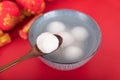A bowl of dumplings or Yuanxiao on a festive red background with a spoon