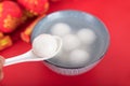 A bowl of dumplings or Yuanxiao on a festive red background with a spoon