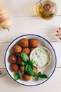 Bowl of falafel with tzatziki sauce on a white wooden table