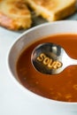 A bowl filled with alphabet tomato soup and the word soup in the spoon.