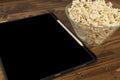 Bowl filled with modern tablet computer and popcorn eaten while watching movies and TV series on wooden floor.