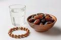 a bowl of dates, a prayer beads, a glass and a copy of the Holy Quran over white background Royalty Free Stock Photo