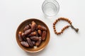 a bowl of dates, a prayer beads, a glass and a copy of the Holy Quran over white background Royalty Free Stock Photo