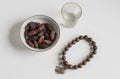 a bowl of dates, a prayer beads, a glass and a copy of the Holy Quran over white background Royalty Free Stock Photo