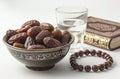 a bowl of dates, a prayer beads, a glass and a copy of the Holy Quran over white background Royalty Free Stock Photo