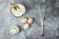 Bowl of flour, eggs and whisker on marble surface