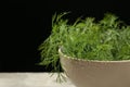 Bowl of fresh green dill with water drops on light grey table against black background, closeup. Space for text Royalty Free Stock Photo