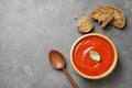 Bowl of fresh homemade tomato soup and bread on grey background, top view.