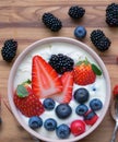 Bowl of fresh mixed berries and yogurt with farm fresh strawberries, blackberries and blueberries served on a wooden table Royalty Free Stock Photo