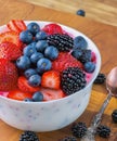 Bowl of fresh mixed berries and yogurt with farm fresh strawberries, blackberries and blueberries served on a wooden table Royalty Free Stock Photo