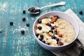 Bowl of fresh oatmeal porridge with banana, blueberries, almonds, coconut and caramel sauce on teal rustic table