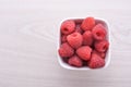 Bowl of fresh raspberries with green leaves on wooden background. Top view Royalty Free Stock Photo