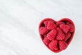 Bowl of fresh red raspberries for dessert, red heart shaped ceramic bowl, white marble background Royalty Free Stock Photo