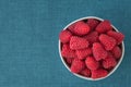 Bowl of fresh red raspberries for dessert, round white ceramic bowl, blue fabric background Royalty Free Stock Photo